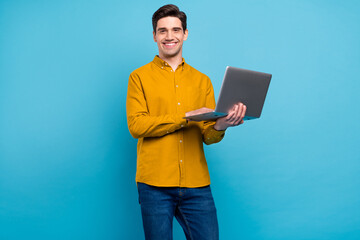 Photo of positive cheerful guy hold laptop beaming smile wear yellow shirt isolated blue color background