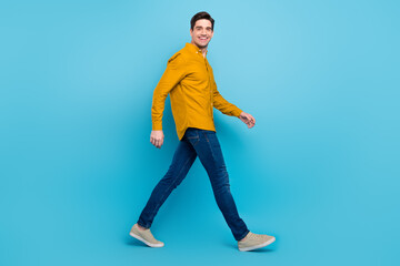 Photo of carefree worker guy move travel toothy smile wear yellow shirt jeans footwear isolated blue color background
