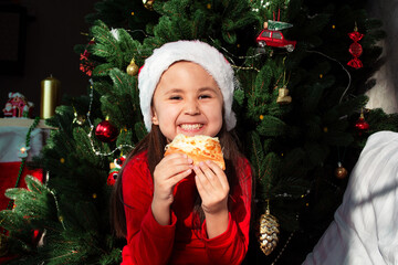 Close Up of little happy girl wearing santa hat eating pizza against the background of the...