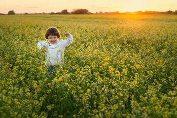 Fototapeta premium a cute little boy with long hair runs and jumps in a blooming field, smiles and laughs, he is happy