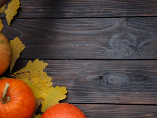 Orange pumpkins, yellow oak leaves on dark wooden table background. Top view, copy space. Autumn, holiday, thanksgiving, harvest season concept.