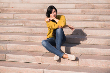 Beautiful and attractive caucasian brunette girl in a yellow sweater posing while sitting on the steps.