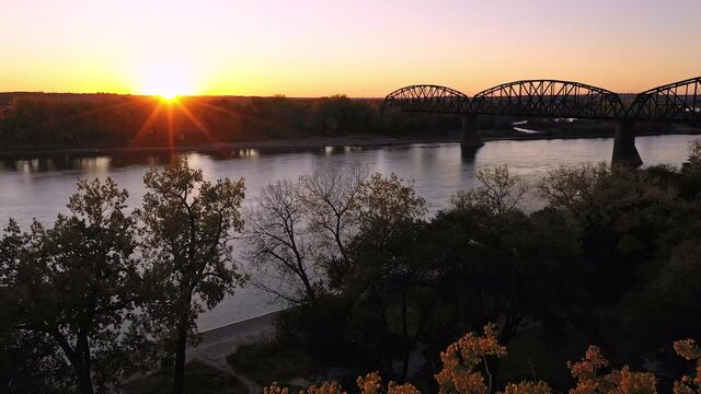 Flying towards the sun setting over North Dakota along the Missouri River with historic old railway bridge spanning the water.