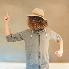 man pointing finger upwards with long hair in front of face with red sunglasses wearing a hat and...