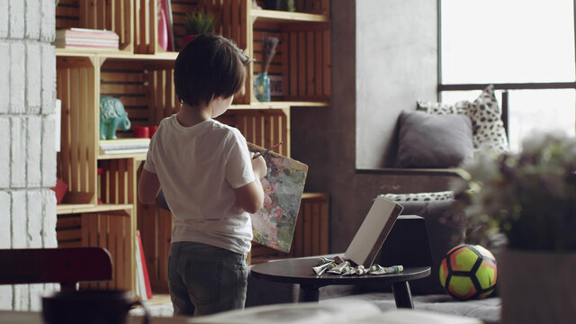 Back view of cute caucasian kid painting on canvas in living room