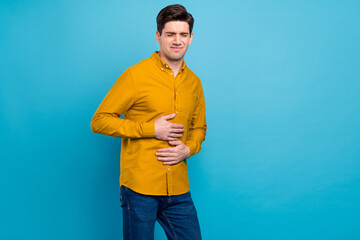 Photo of tired exhausted guy hands belly suffer stomachache wear yellow shirt isolated blue color...