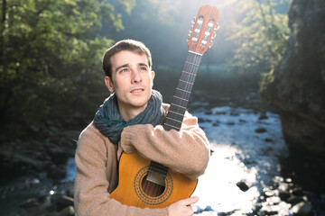 Young musician holding a guitar beside a river