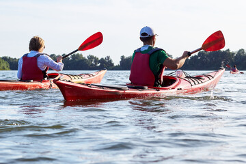 Happy young couple in two kayaks paddle at river at summer time. Back view