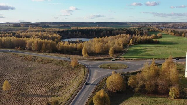 Aerial view of the autumn city and the road. Roundabout for cars. Cars drive along the road. Homes and shops. Yellow and orange trees, green grass. 4K drone video.