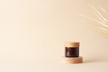 Jar of cosmetic cream with wood podium and palm leaf on pastel beige background. Close up, copy space
