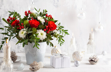 Festive winter flower arrangement in vase and Christmas decorations on table.