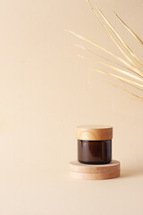 Jar of cosmetic cream with wood podium and palm leaf on pastel beige background. Close up, copy...