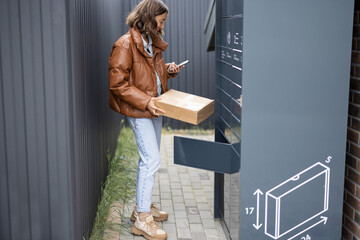Young caucasian woman putting parcel to cell of automatic post terminal. Smiling girl holding...