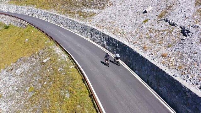 Aerial drone footage following cyclists that bike along the famous Stelvio mountain pass in the alps in Italy on a sunny summer day. 