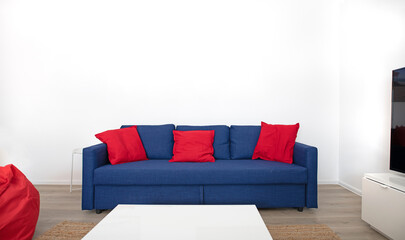 Blue sofa with red cushions in front of white wall