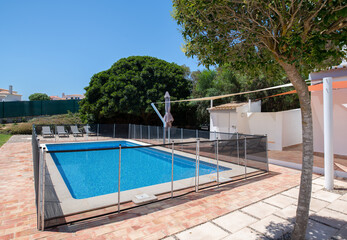 Fenced swimming pool with brick tiled surround in the garden of a white villa