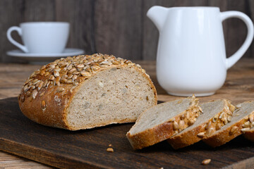 Homemade sliced bread on dark cutting board, cup and milk jug on wooden table