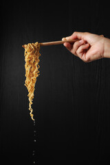 Hand holding chopsticks and noodles on black background