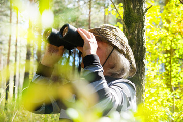 Blurred active senior woman with binoculars in the forest