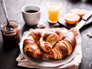 Gebackene Croissants auf einem Teller, eine Tasse Kaffee und Orangensaft auf einem Holz Tisch. Frankreich, Frühstück.