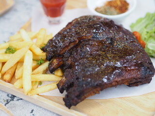 Pork Spareribs BBQ, Barbeque Pork Ribs with french fries vegetable salad, tomato sauce in a clear glass on wooden tray, food