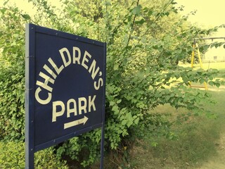 Children's park sign with a green background in a yellow sky. 