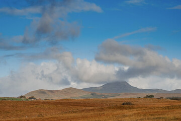 Vast empty field and Croagh Patrick mountains with clouds look like volcano eruption. Stunning Irish landscape. Beautiful nature scene with blue cloudy sky. County Mayo, Ireland