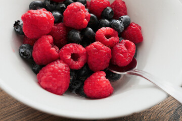 Raspberry and blueberry in a white bowl on a wooden table. Healthy fruit mix. Produce product. Healthy diet choice.