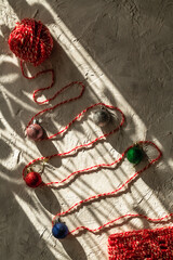 A Christmas tree with red threads and colored balls and a knitted bag on a light background.
