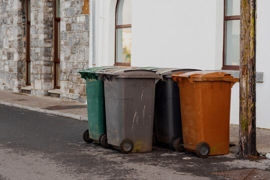 Four wheelie bins of different color and waste left in a street for collection. Waste and recycle management industry