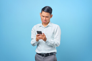 Portrait of a sad young handsome businessman using smartphone on blue background