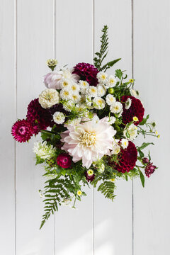 Bouquet made of dahlias, strawflowers and other summer flowers on a white wooden background.