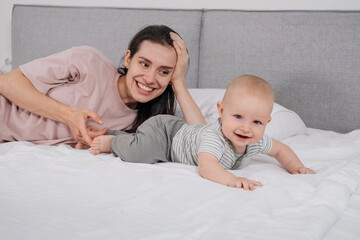 Mother with baby boy cuddling in bed in the morning. Happy time with cute infant at home, playing...
