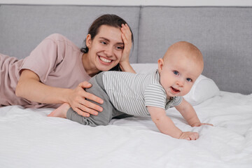 Mother with baby boy cuddling in bed in the morning. Happy time with cute infant at home, playing...