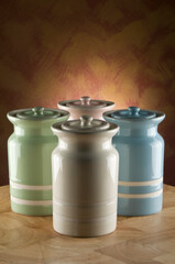 Four colourful ceramic canisters on timber bench with rustic background