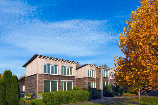 modernes mit L&auml;rche vert&auml;feltes zweiteiliges zweigeschossiges Holz-Passivhaus mit Pultdach im Herbst