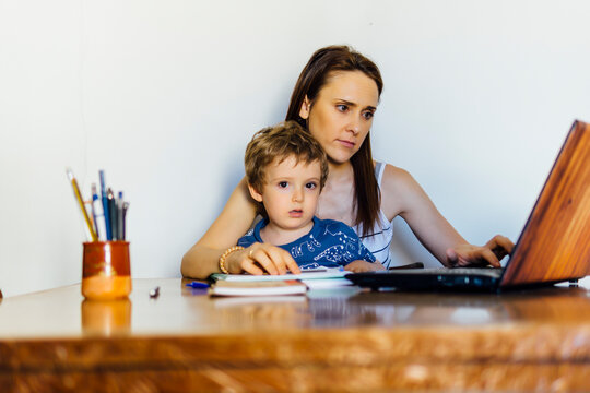 beautiful middle-aged young woman at home sitting at a table with computer with her three-year-old son caught.concept telework.maternity. conciliation