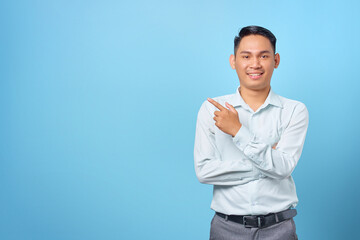 Smiling young handsome businessman pointing finger away at copy space on blue background