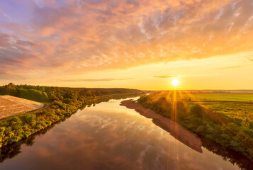 Fototapeta na wymiar amazing view at beautiful summer river sunset, halo with reflection on water with green bushes, calm water ,deep colorful cloudy sky and glow on horizon on a background, spring evening landscape