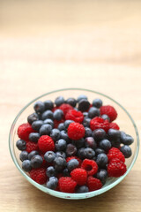Glass bowl filled with raspberries and blueberries on wooden table. Selective focus.