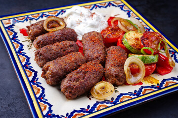 Traditionelle kroatische Cevapi als würzige Fleischbällchen mit Barbecue Gemüse und Zaziki serviert als close-up auf einem rustikalen Teller  - obrazy, fototapety, plakaty
