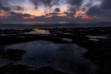 Fototapeta premium amazing scenic view at a sea shore from a coast after dramatic colorful sunset with flying blured clouds and reflection on water surface , beautiful ocean landscape