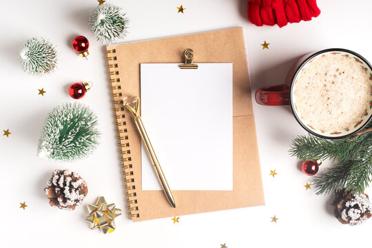 Desktop blank note pad. Flat lay of white working table background with cup of coffee and Christmas decoration. Top view balls, fir tree, paper clips, mock up greeting card, craft Notebook and pen.