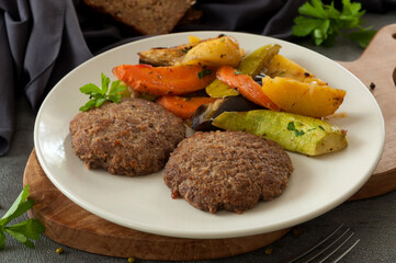 beef patties with baked vegetables on a gray plate