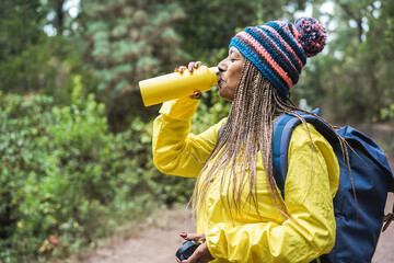 Senior african woman drinking water during trekking day into the woods - Travel concept - Focus on...