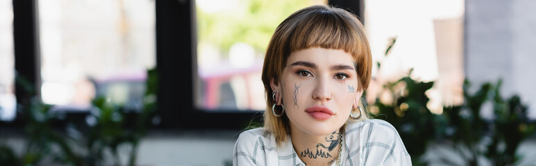 young businesswoman with tattoo and piercing looking at camera in office, banner