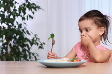 Cute little girl refusing to eat her breakfast at home, space for text