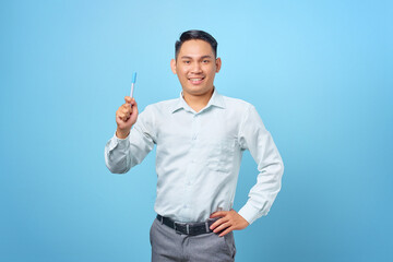 Happy young handsome businessman having a creative idea and holding pen on blue background