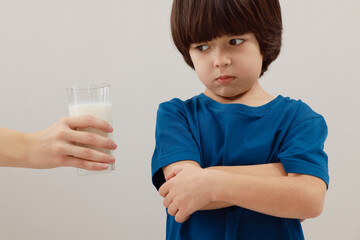 Cute little boy refusing to drink milk on grey background