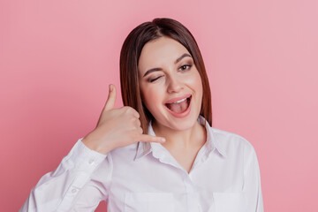 Photo of young cheerful lady show finger call me sign wink eye flirty isolated over pink color background